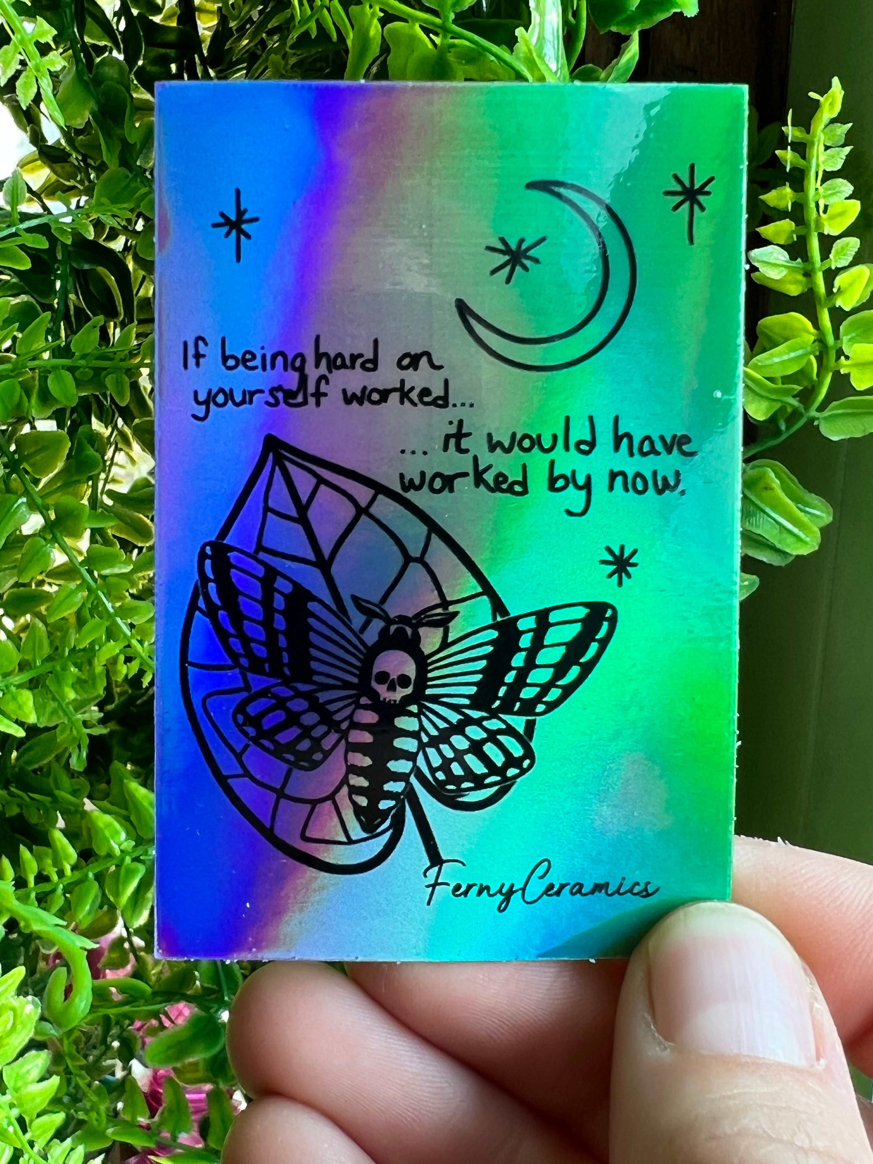 A resilient hand holding a Ferny Ceramics 2x3 Rectangular Holographic Sticker.