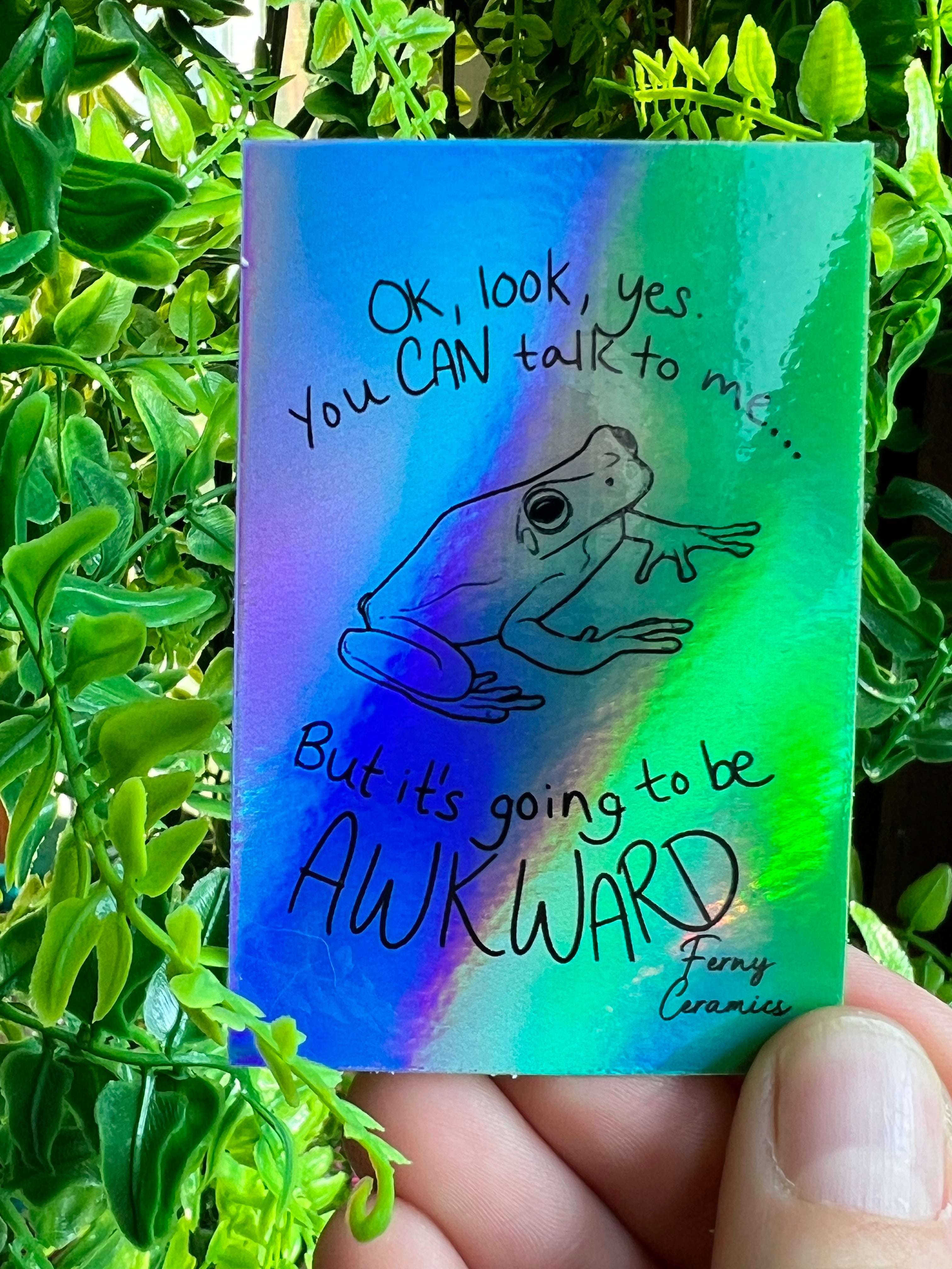 A person holding a Ferny Ceramics 2x3 Rectangular Holographic Sticker that says on look you can talk to me but it&