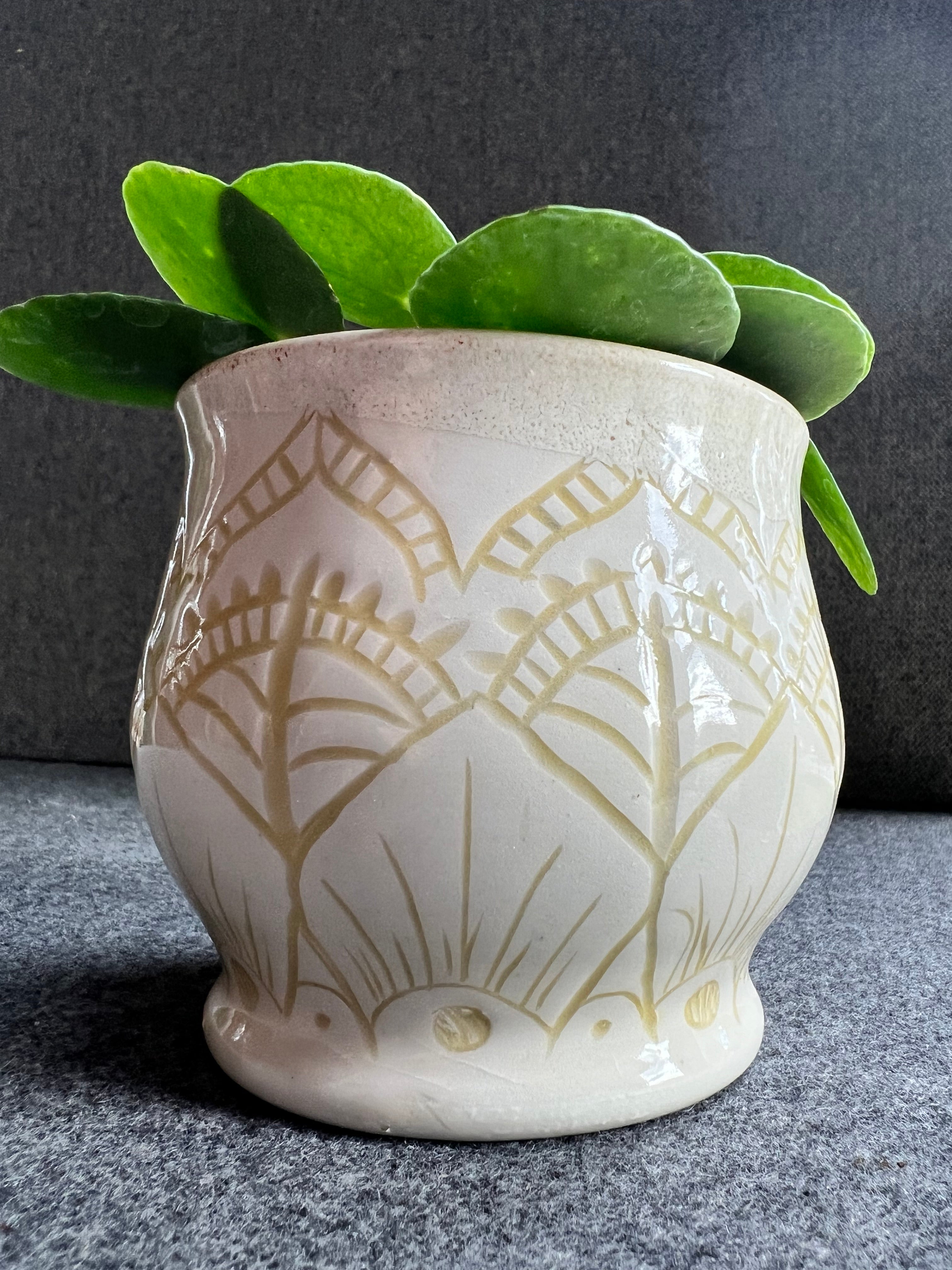 A white ceramic pot with abstract carvings is inlaid with a creamy yellow underglaze.