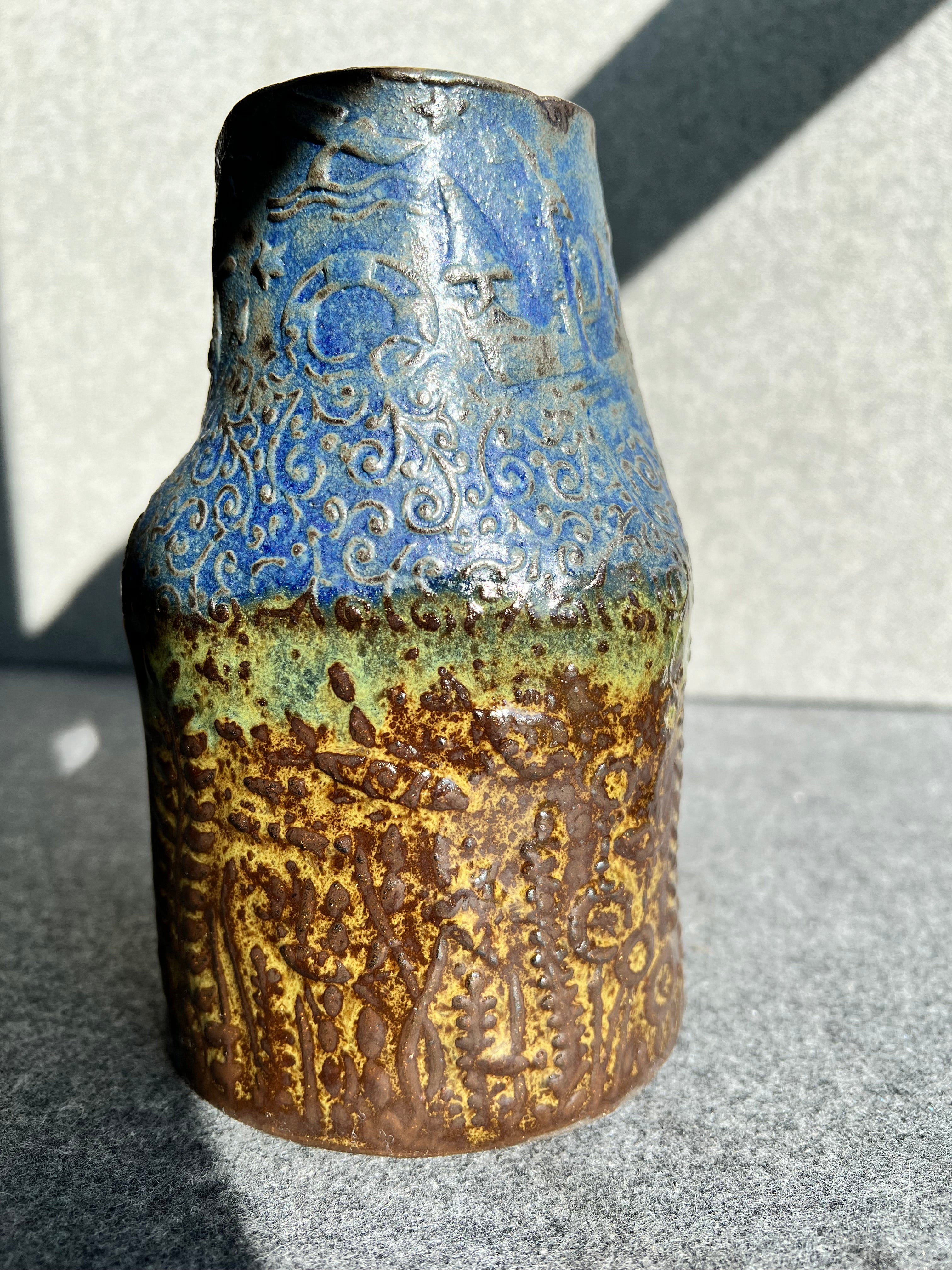 a three sided, handbill, green, brown, and blue ocean themed vase sits in front of a grey background.