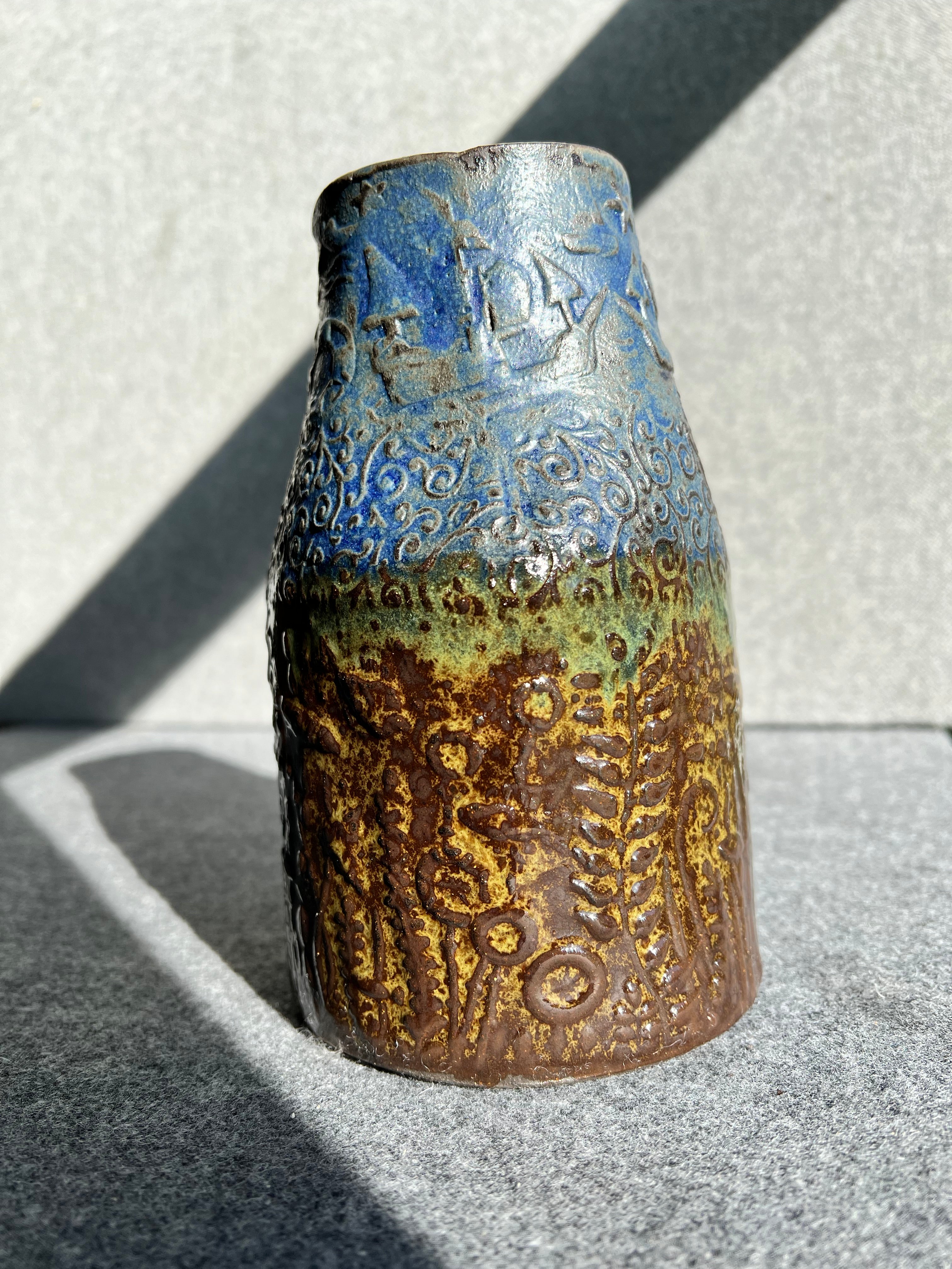 a three sided, handbill, green, brown, and blue ocean themed vase sits in front of a grey background.