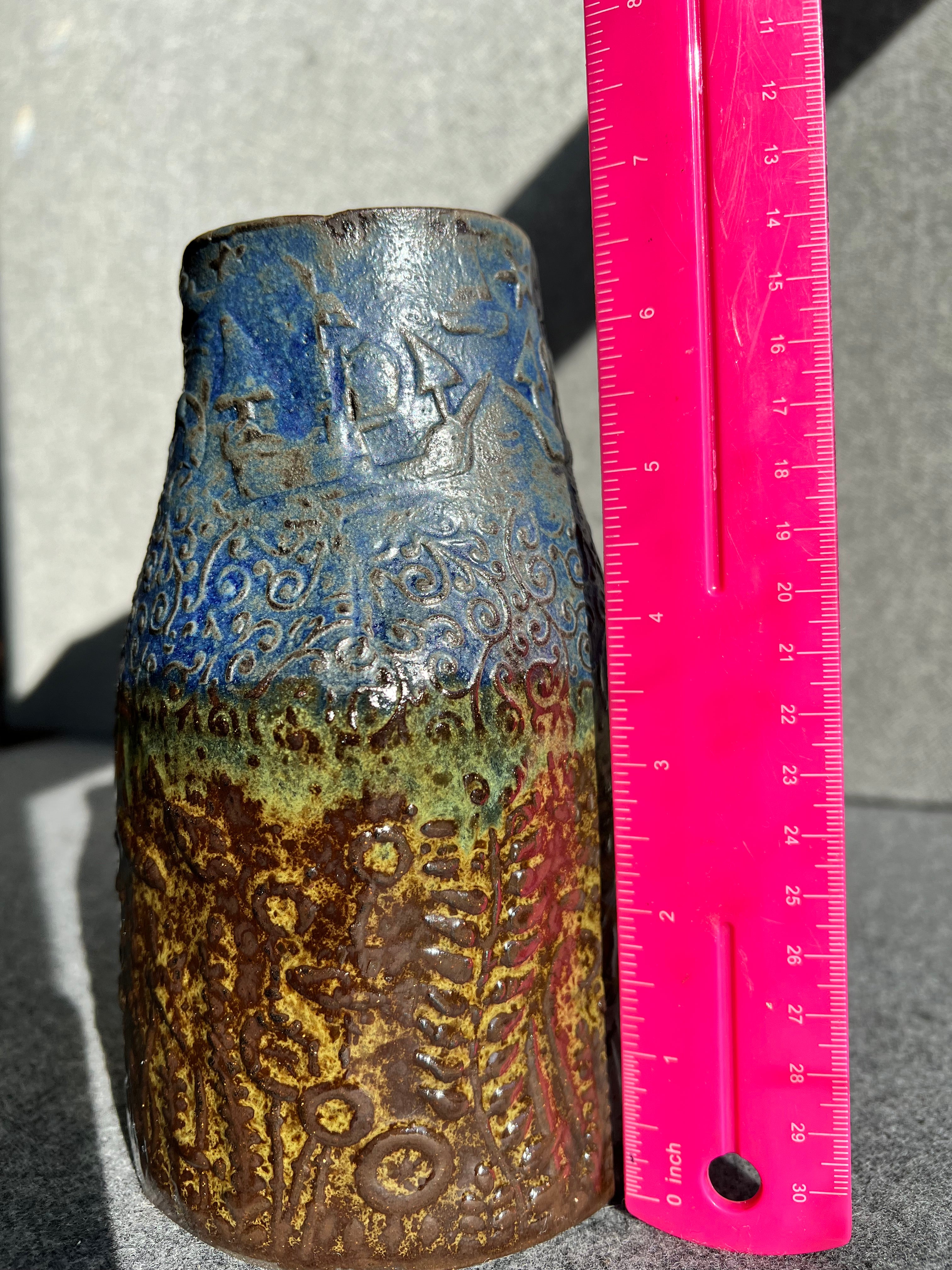 a three sided, brown, green, and blue vase with an ocean theme sits next to a bright pink ruler. The vase is 6.75 inches tall.