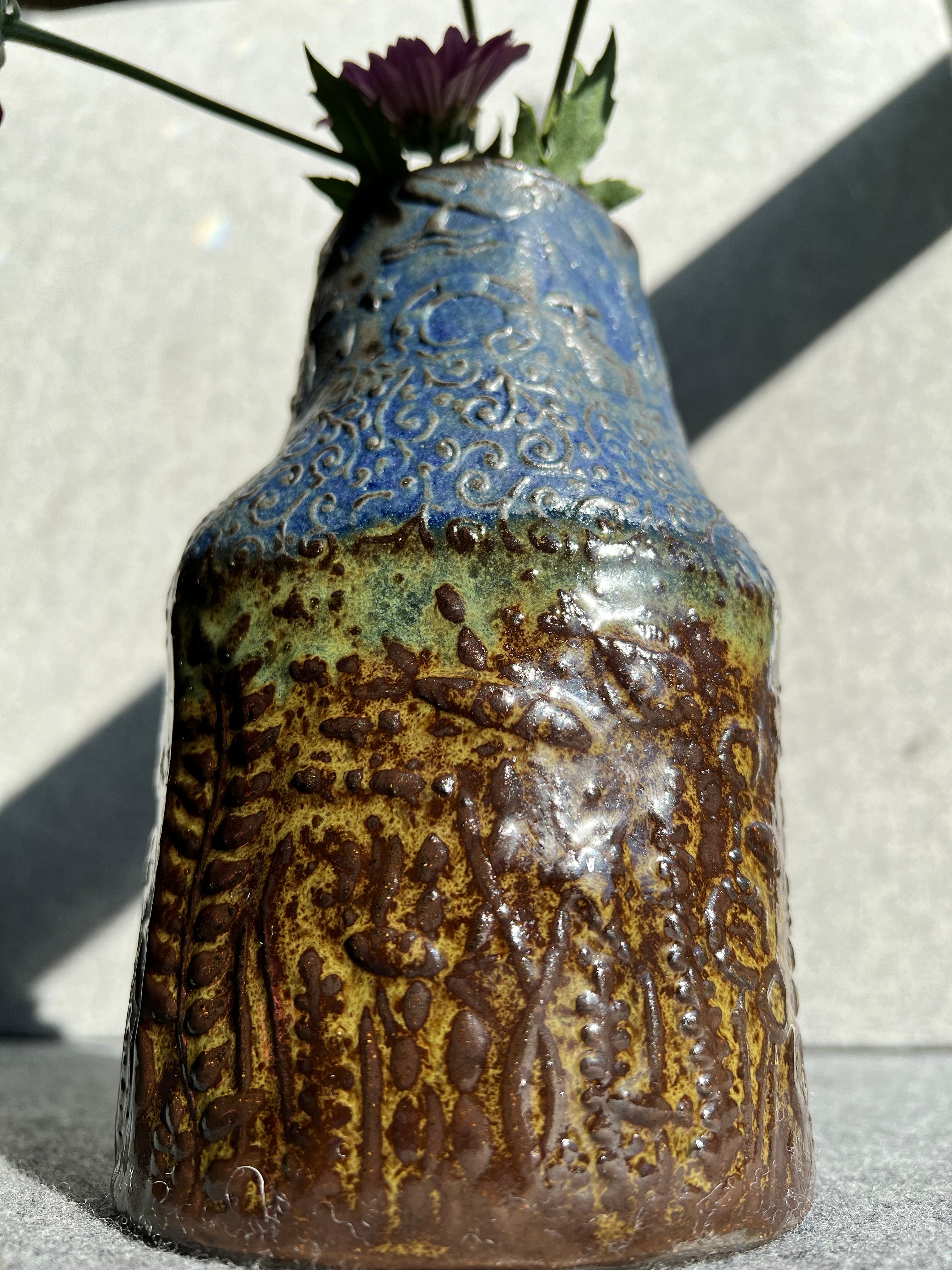 an up close view of a three sided, handbill, green, brown, and blue ocean themed vase sits in front of a grey background.