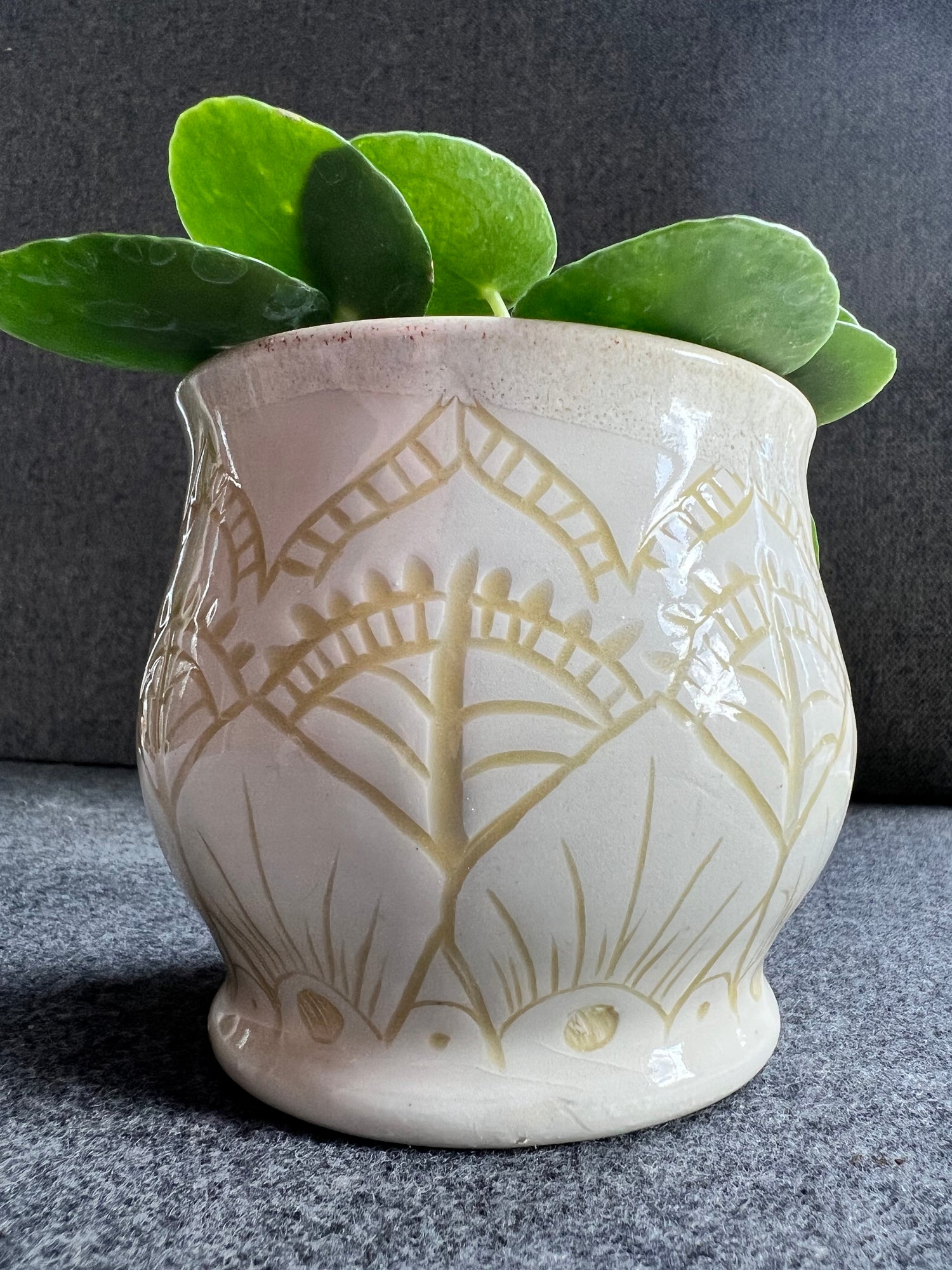 A white ceramic pot with abstract carvings is inlaid with a creamy yellow underglaze.